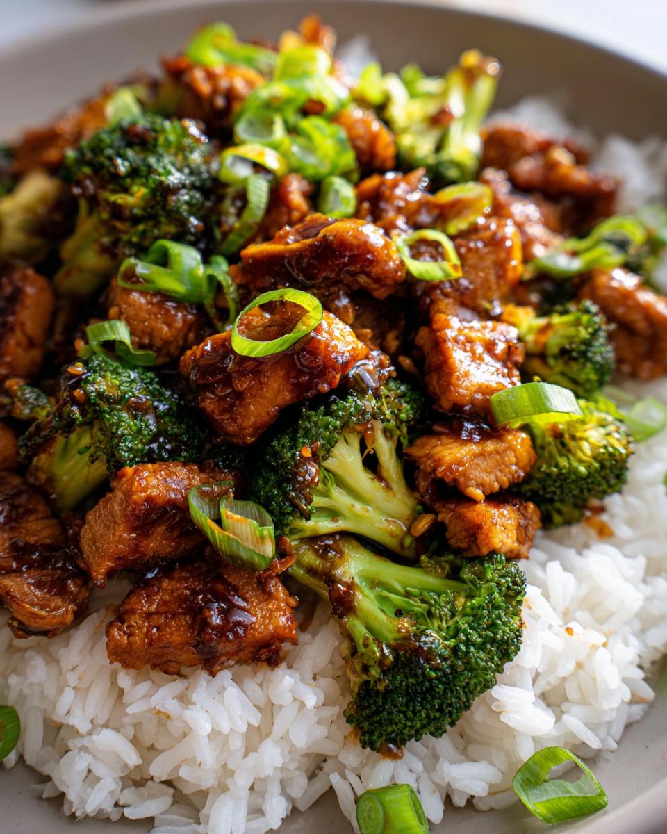 Close-up of a bowl of Chicken and Broccoli Stir Fry served over white rice, garnished with green onions.