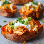 Close-up of a Chicken Enchilada Stuffed Sweet Potato topped with cheese, sour cream, and green onions.
