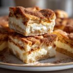 Close-up of stacked Churro Cheesecake Bars, featuring layers of creamy cheesecake filling and a cinnamon sugar topping.
