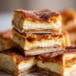 Close-up of stacked Churro Cheesecake Bars, featuring layers of creamy cheesecake and a cinnamon sugar topping.