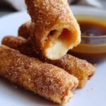 A close-up of Cream Cheese Churro Rollups, showing a gooey cream cheese filling spilling out of one roll.