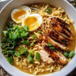 A bowl of Creamy Garlic Chicken Ramen featuring noodles, sliced grilled chicken, soft-boiled eggs, and chopped green onions.