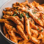 Close-up of a bowl filled with Creamy Tomato Basil Pasta, garnished with fresh herbs and grated cheese.