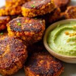 A close-up shot of golden-brown Crispy Sweet Potato Patties served with a vibrant green avocado dip.