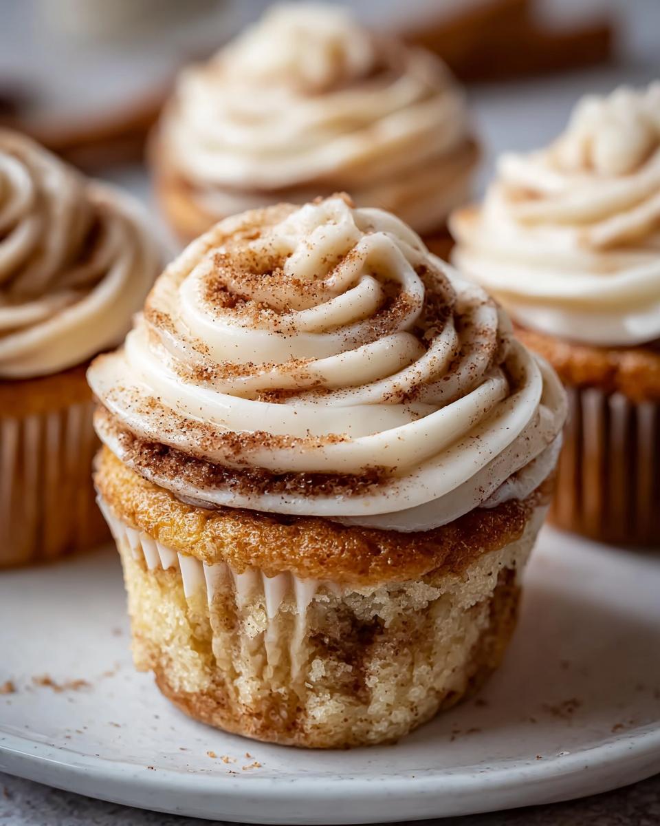 Close-up of a Delicious Cinnamon Roll Cupcake topped with swirled cream cheese frosting and a sprinkle of cinnamon.