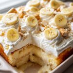 A slice of easy banana pudding poke cake overflowing with creamy pudding and topped with whipped cream and banana slices.