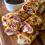 Close-up of Easy French Dip Tortilla Roll-Ups filled with ham and melted cheese, served with a side of au jus.