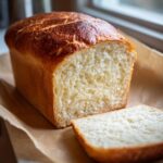 A golden-brown loaf of fluffy keto sandwich bread with one slice cut, showcasing its soft interior.