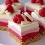 A close-up of a slice of Frozen White Chocolate Raspberry Bars, featuring layers of raspberry and white chocolate mousse on a cookie crust, topped with fresh raspberries and white chocolate shavings.