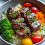 A close-up of Garlic Butter Steak Bite Bowls featuring tender steak bites, rice, broccoli, cherry tomatoes, and shredded carrots.