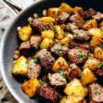 Close-up of Garlic Steak Bites with Potatoes Skillet in a pan, seasoned with herbs.