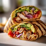 Close-up of a delicious Grilled California Chicken Wrap with Avocado, sliced in half to show grilled chicken, avocado, lettuce, tomato, and red onion.