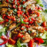 A vibrant Grilled Chicken Bruschetta Salad featuring sliced grilled chicken, fresh tomatoes, basil, and red onion on a bed of lettuce.