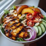 A vibrant Grilled Peach Chicken Salad Summer Bowl with grilled chicken, sliced peaches, tomatoes, cucumber, red onion, and almonds.
