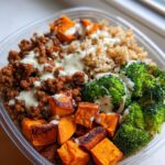 A close-up of a Ground Turkey Sweet Potato Meal Prep Bowl featuring seasoned ground turkey, roasted sweet potato cubes, brown rice, and broccoli florets, drizzled with a creamy sauce.