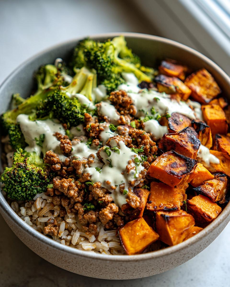 A close-up of a Ground Turkey Sweet Potato Meal Prep Bowl featuring rice, seasoned ground turkey, roasted sweet potatoes, and steamed broccoli with a creamy dressing.