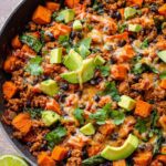 A close-up of a Ground Turkey Sweet Potato Taco Skillet, featuring ground turkey, sweet potato cubes, black beans, spinach, melted cheese, avocado, and cilantro.