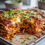 A delicious slice of High Protein Chicken Enchilada Casserole, showing layers of tortillas, shredded chicken, beans, corn, and melted cheese.
