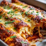 Close-up of cheesy High Protein Chicken Enchiladas in a baking dish, with melted cheese stretching.
