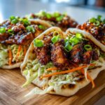 Close-up of delicious Honey Garlic Naan Chicken Tacos filled with shredded cabbage, carrots, and glazed chicken pieces, garnished with green onions.
