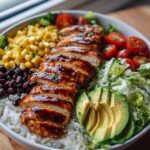A vibrant Honey Lime Chicken Avocado Bowl filled with rice, black beans, corn, tomatoes, lettuce, and sliced avocado.