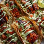 Close-up of Honey Lime Chicken Tacos topped with avocado crema, cilantro, and a lime wedge.