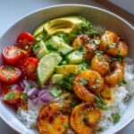 Close-up of a Honey Lime Shrimp Avocado Bowl Easy Fresh Dinner with rice, shrimp, avocado, cherry tomatoes, cucumber, red onion, and lime.