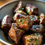 Close-up of Irresistible Crockpot Steak Bites, glistening with sauce and herbs in a bowl.