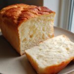 A close-up of a soft and fluffy Keto Bread Loaf, with one slice cut and placed on a plate.