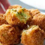 Close-up of crispy Keto Broccoli Cheddar Bites, with one bite broken open to reveal melted cheese and broccoli.