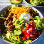 A delicious bowl of Keto Taco Salad Recipe with seasoned ground beef, shredded lettuce, cheese, guacamole, and pico de gallo.