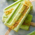Close-up of refreshing Key Lime Pie Popsicles Recipe, topped with graham cracker crumbs and lime slices in the background.