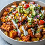 A close-up of Loaded Southwest Potato Bowls featuring seasoned chicken, crispy potatoes, black beans, corn, avocado, and a drizzle of crema.