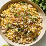 A bowl of Mexican Street Corn Pasta Salad with Chicken, topped with crumbled cheese, cilantro, and chili flakes.