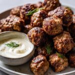 A close-up of a plate filled with golden-brown Mini Greek Meatball Bites, served with a creamy dill dip.