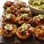 Close-up of Nacho Loaded Potato Skins Recipe, topped with cheese, sour cream, tomatoes, and green onions.