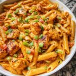 Close-up of a bowl of One Pot Creamy Cajun Chicken Pasta, featuring penne pasta, chicken pieces, and green onions.