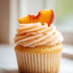 A single Peach Bellini Cupcake topped with swirled peach frosting and a fresh peach slice.