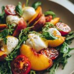 A vibrant Peach Caprese Salad with creamy burrata, ripe tomatoes, fresh peaches, and basil leaves.