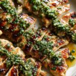 Close-up of sliced Peach Tea Grilled Chicken topped with a vibrant green herb sauce.