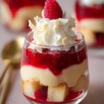 Close-up of a Raspberry White Chocolate Mini Trifles Dessert in a glass, topped with whipped cream and a raspberry.