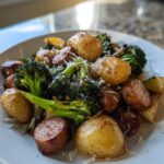 A close-up of a white plate filled with a Sheet Pan Sausage Potatoes and Broccoli Dinner, topped with grated cheese.