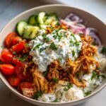 A delicious bowl of slow cooker chicken gyros meal prep, featuring shredded chicken, rice, tomatoes, cucumbers, red onion, and tzatziki sauce.