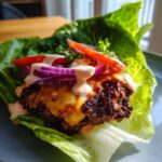 A delicious Smash Burger Lettuce Wrap with melted cheese, red onion, tomato, and sauce on crisp lettuce leaves.