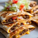 Close-up of a stack of crispy Smashburger Quesadillas filled with seasoned ground beef and melted cheese, topped with fresh lettuce and tomato.