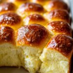 Close-up of golden-brown, fluffy Soft Brioche Dinner Rolls, with one roll pulled apart to show its airy texture.