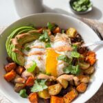 A hearty Southwest Breakfast Bowl featuring roasted vegetables, a sunny-side-up egg, sliced avocado, and a drizzle of sauce.