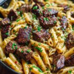 Close-up of a skillet filled with steak bites garlic butter pasta, garnished with fresh parsley.