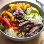 A delicious bowl of Steak Fajita Bowls with Garlic Lime Rice, featuring grilled steak, peppers, corn, beans, avocado, and sour cream.