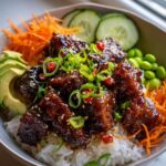 Close-up of a delicious Sticky Chicken Poke Bowl with rice, avocado, shredded carrots, edamame, and chili peppers.